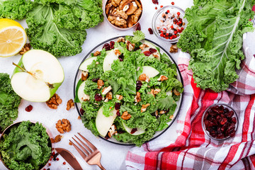 Kale salad with dried cranberry, green apples and walnuts. Healthy vegan food, top view, grey...