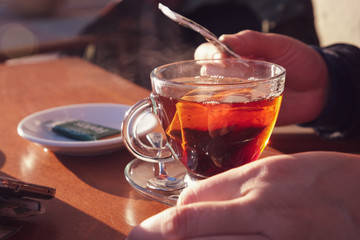 Tea cup on table with man's hands at the sides, outdoors at sunset.