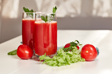 Two glasses with fresh tomato juice and ripe tomatoes on white table near window.