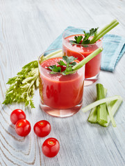 Two glasses with fresh tomato juice and ripe tomatoes  on light wooden background. Top view