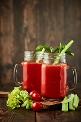 Two glasses with fresh tomato juice, celery, parsley and ripe tomatoes on dark brown wooden background.