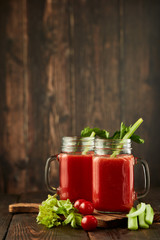 Two glasses with fresh tomato juice, celery, parsley and ripe tomatoes on dark brown wooden background.