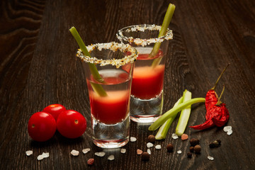 Two shot glasses with cocktail Bloody Mary on dark wooden background