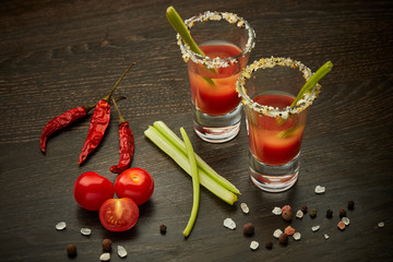 Two shot glasses with cocktail Bloody Mary on dark wooden background