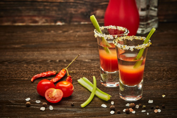 Two shot glasses with cocktail Bloody Mary on dark wooden background with copy space