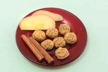 Cinnamon apple mini cookies with apple slices and cinnamon sticks on red glass dessert plate on green background