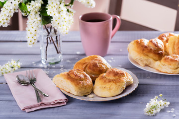sweet buns on ceramic plate, blossom branches on white wooden background