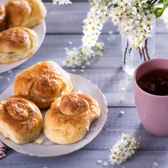 sweet buns on ceramic plate, blossom branches on white wooden background