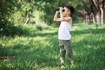 Naklejka na ściany i meble little boy use binoculars in summer garden on warm day outdoors..