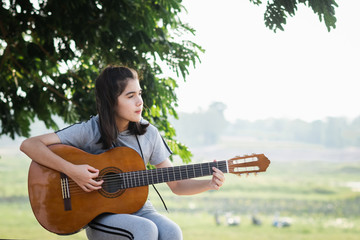 Beautiful young woman playing guitar at sunset, fashion lifestyle