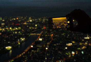 A person taking pictures of the Tokyo night view from Tokyo Sky Tree with his smartphone.