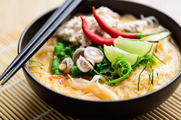 Spicy rice noodles soup with spices and herbs (Thai Tom Yum) in a bowl with chopsticks, Asian food	