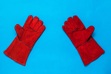 Bright red welding gloves on a blue background.