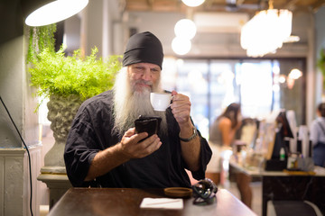 Mature bearded hipster man drinking coffee and using phone at the coffee shop