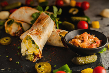 mexican food background of chicken and cheese burritos with vegetable on stone plate in dark tone, selective focused