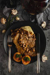 food background of pork chop steak with champignon sauce served with mash potato in black dish on table with red wine in dark tone, selective focused