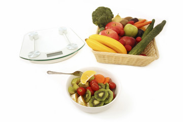 A basket of fruits and vegetables, a bowl of fruit and vegetable salad and a weight scale