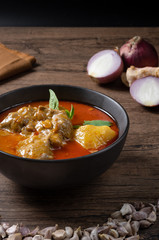 Chicken massaman curry in black bowl with herb and spices on wooden background. Thai authentic food called massaman kai.