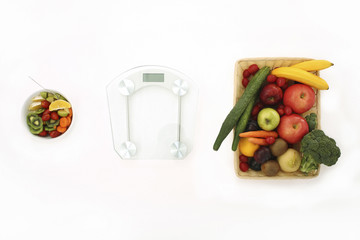 A weight scale in between a basket of fruits and vegetables and a bowl of salad