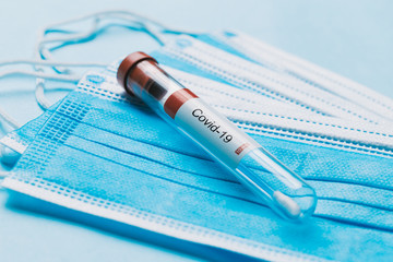 One single glass test tube containing a Corona virus test swab sitting on top of some blue surgical masks 