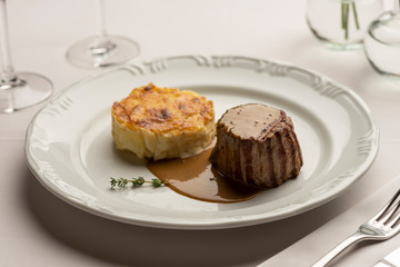 Fillet mignon tenderloin with potatoes gratin and green poivre vert sauce gravy on white with wine and water glass.
