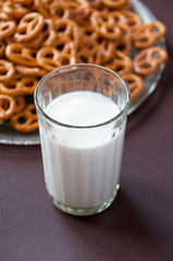 A glass of milk and pretzel cookies in a transparent plate on a brown background