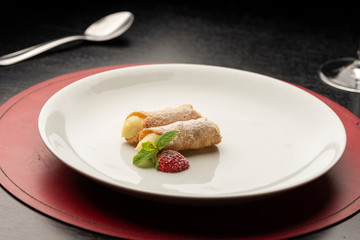 Cannoli stuffed with cream and strawberry mint on white plate dark background