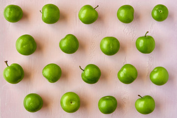 Colorful fruit pattern of fresh green sour plums on pastel pink background . Top view, flat lay