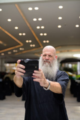 Mature handsome bald bearded man taking selfie in the city outdoors