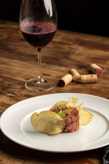 Steak tartare with potato chips on white plate and wooden table