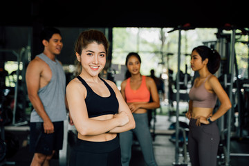 Fototapeta na wymiar Joyful young healthy Chinese Asian female trainer looking at camera while standing with multiracial friends in gym