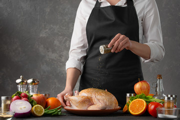 Chef cooks chicken, sprinkles with seasonings. Against the background of vegetables and fruits. Delicious and wholesome food. With space for an inscription.