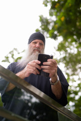 Mature bearded hipster man looking serious while using phone outside the subway train station