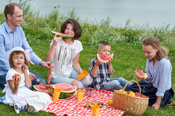 Happy family eating watermelon at a picnic. Young friends and their children in nature