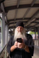 Mature handsome bearded hipster man using phone at footbridge in the city