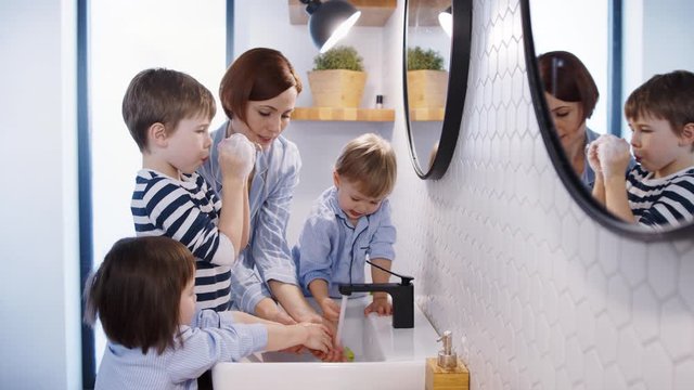 Mother with small children in pajamas in bathroom at home, washing hands.
