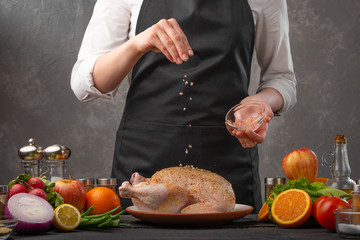 Cooking chicken by the chef sprinkling with coarse sea salt on a background of vegetables. Cookbook, and recipe book