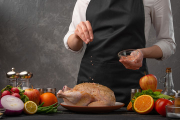 Cooking chicken by the chef sprinkling with coarse sea salt on a background of vegetables. Cookbook, and recipe book