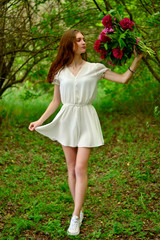 Slender brown-haired woman in a white dress with peonies in her hands