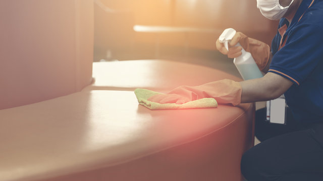 Woman hand in protective orange rubber gloves holding green microfiber cleaning cloth and wiping dust using a spray sterilizing solution make cleaning and disinfection for good hygiene