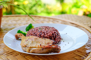 Close up grilled chicken with rice on white plate on wooden table.