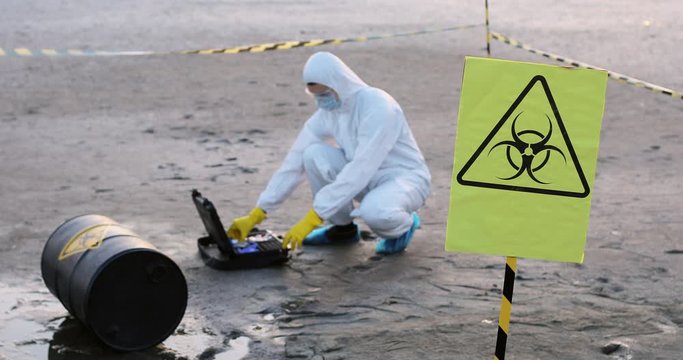 A scientist in a protective suit opens a portable laboratory, in the foreground is a biohazard sign.