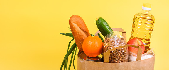 Paper bag with food supplies for the period of quarantine isolation on a yellow background. Copyspace.