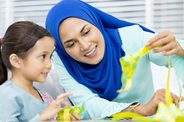 Muslim woman guiding her daughter in weaving ribbon ketupats