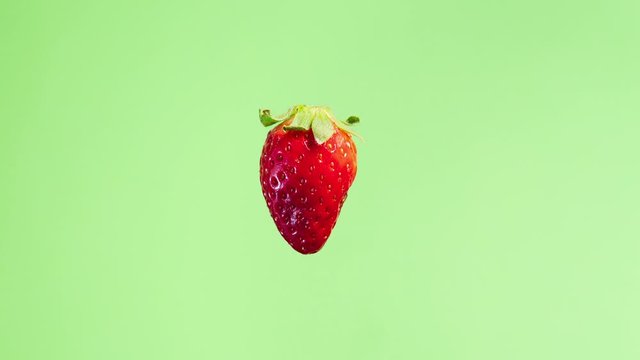 4K stop motion video of a fresh strawberry getting bigger in the frame with green background. Straberry zoom effect screensaver. Summer  fruit animation