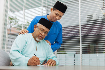 Muslim man writing a greeting card with his son