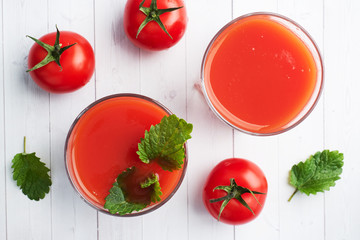 Tomato juice in glass glasses and fresh ripe tomatoes on a branch. White wooden background with copy space.