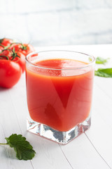 Tomato juice in glass glasses and fresh ripe tomatoes on a branch. White wooden background with copy space.