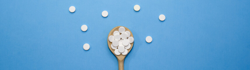 White pills are scattered on a blue background. White drugs on a wooden spoon. Treatment of patients for the virus. Strengthening the immune system. Web banner.