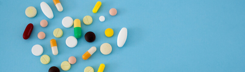 Beautiful image of colorful pills and capsules on a blue background. prevention of coronavirus. Web banner on  site with empty space for text on the right side. Isolated. Medical preparations closeup